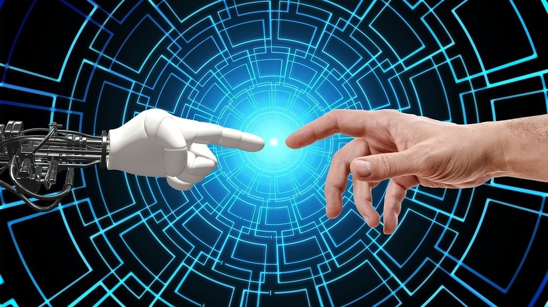 A visualization of human-AI collaboration showing a human hand and robotic hand reaching toward each other against a blue technological background with digital circuit patterns. This representation effectively symbolizes the integration of AI with human workers in modern workplaces.